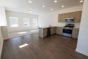Kitchen featuring open floor plan, a peninsula, appliances with stainless steel finishes, dark wood-style floors, and recessed lighting