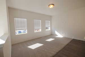 Carpeted spare room featuring baseboards and wood finished floors