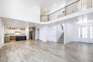Unfurnished living room featuring recessed lighting, a high ceiling, light wood finished floors, a chandelier, and stairway