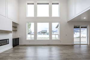 Unfurnished living room with a glass covered fireplace, a towering ceiling, and light wood-style floors