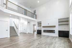 Unfurnished living room featuring a high ceiling, a glass covered fireplace, recessed lighting, light wood finished floors, and stairs