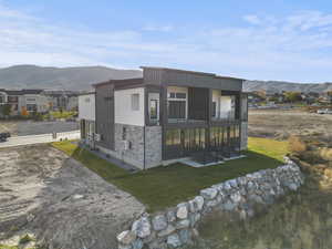 View of side of property featuring a mountain view, stone siding, a lawn, a balcony, and board and batten siding