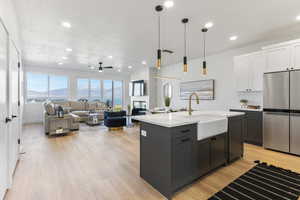 Kitchen featuring white cabinetry, a kitchen island with sink, freestanding refrigerator, a multi sided fireplace, and decorative light fixtures
