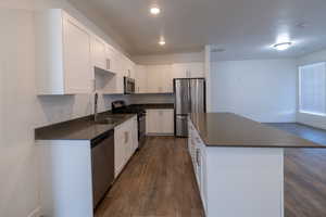 Kitchen with stainless steel appliances, dark wood finished floors, white cabinetry, a center island, and recessed lighting
