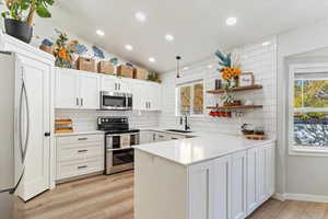 Kitchen with stainless steel appliances, hanging light fixtures, light wood-style floors, backsplash, and white cabinetry