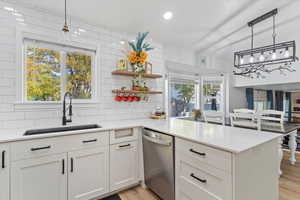 Kitchen with hanging light fixtures, dishwasher, a peninsula, tasteful backsplash, and light wood finished floors