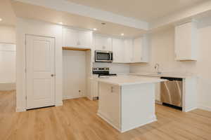 Kitchen with recessed lighting, white cabinets, stainless steel appliances, light wood finished floors, and a center island