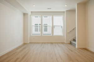 Unfurnished living room featuring stairs and light wood-style floors
