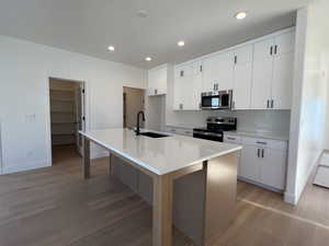 Kitchen featuring a center island with sink, appliances with stainless steel finishes, light wood-style floors, white cabinetry, and recessed lighting