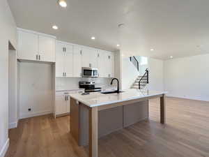 Kitchen featuring light wood-type flooring, white cabinetry, stainless steel appliances, recessed lighting, and a center island with sink