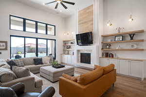 Living room with light wood-style floors, a towering ceiling, a fireplace, ceiling fan, and recessed lighting