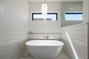 Bathroom with marble finish flooring, a freestanding bath, wainscoting, and a chandelier