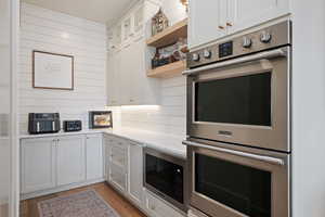 Kitchen featuring appliances with stainless steel finishes, white cabinets, open shelves, glass insert cabinets, and wooden walls