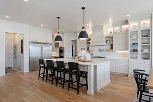 Kitchen with white cabinetry, appliances with stainless steel finishes, a kitchen bar, decorative light fixtures, and a center island with sink