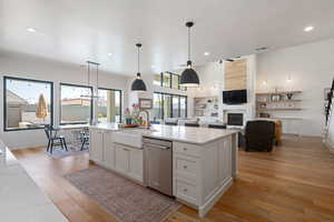 Kitchen featuring open floor plan, hanging light fixtures, light wood-style floors, light stone countertops, and white cabinets