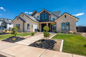 View of front of house with a front yard, stone siding, board and batten siding, and covered porch