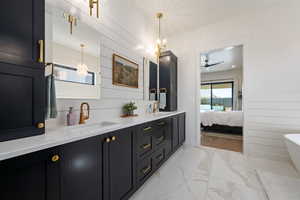 Ensuite bathroom with double vanity, light marble finish floors, ceiling fan, a soaking tub, and a chandelier