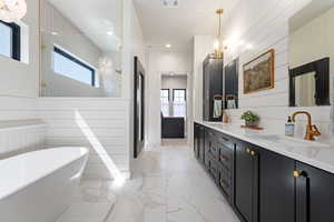 Full bath with light marble finish floors, plenty of natural light, a soaking tub, double vanity, and wooden walls
