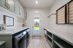Washroom with washing machine and clothes dryer, wood walls, recessed lighting, and cabinet space