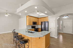 Kitchen with a peninsula, arched walkways, light stone countertops, appliances with stainless steel finishes, and a ceiling fan