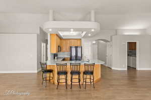 Kitchen with recessed lighting, a peninsula, a kitchen bar, light stone counters, and light wood-style flooring