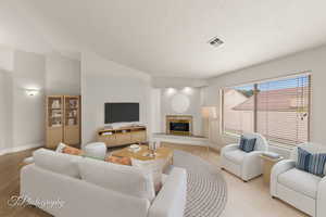Living room with lofted ceiling, a fireplace, light wood finished floors, and a textured ceiling