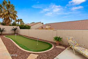 Fenced backyard featuring an area to practice putting and a patio area