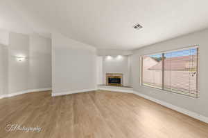 Unfurnished living room featuring a fireplace, light wood-style flooring, a textured ceiling, and lofted ceiling