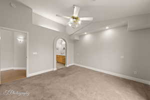 Unfurnished bedroom featuring vaulted ceiling, light carpet, arched walkways, connected bathroom, and a ceiling fan