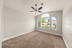 Carpeted empty room featuring lofted ceiling, a textured ceiling, and a ceiling fan
