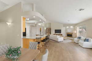 Living room featuring recessed lighting, light wood finished floors, a glass covered fireplace, and vaulted ceiling