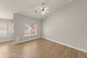 Empty room with vaulted ceiling, light wood finished floors, a textured ceiling, and a ceiling fan