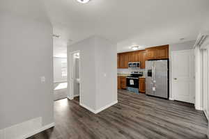 Kitchen with brown cabinetry, appliances with stainless steel finishes, light countertops, and dark wood-style flooring