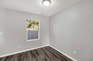Spare room featuring dark wood-style flooring and baseboards