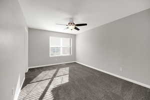 Unfurnished room with dark carpet and a ceiling fan