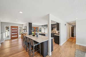 Kitchen featuring light wood-type flooring, recessed lighting, dark brown cabinets, tasteful backsplash, and a kitchen breakfast bar