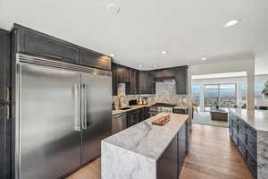 Kitchen featuring a kitchen island, high quality appliances, light stone counters, light wood-style flooring, and recessed lighting