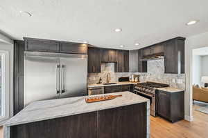 Kitchen with dark brown cabinetry, light stone counters, high end appliances, light wood-style floors, and recessed lighting
