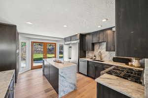 Kitchen with light stone counters, a textured ceiling, a center island, light wood-type flooring, and decorative backsplash