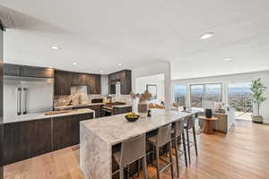 Kitchen with dark brown cabinets, a kitchen bar, light stone countertops, backsplash, and light wood-style floors