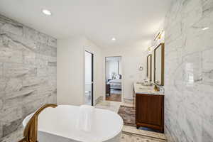 Ensuite bathroom with tile walls, double vanity, a freestanding bath, stone wall, and recessed lighting