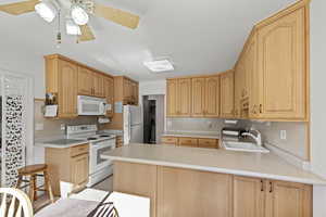 Kitchen featuring a peninsula, white appliances, light countertops, light brown cabinetry, and ceiling fan