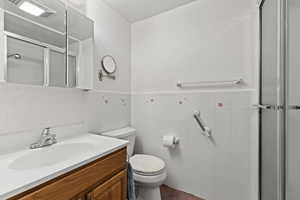 Full bath with a shower stall, vanity, wainscoting, and tile walls