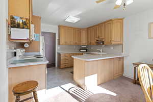 Kitchen with a peninsula, light countertops, white appliances, ceiling fan, and backsplash