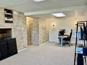 Office space featuring carpet flooring, a paneled ceiling, and brick wall