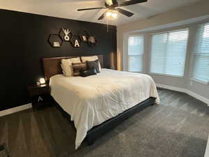 Bedroom with dark colored carpet, multiple windows, and a ceiling fan