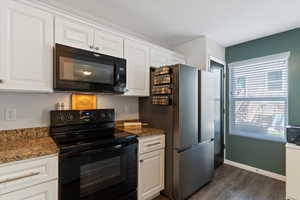 Kitchen with black appliances, white cabinetry, dark wood finished floors, and dark stone counters