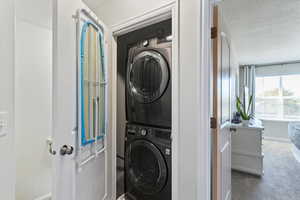 Washroom with a textured ceiling, stacked washer / drying machine, and carpet floors