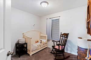 Bedroom featuring dark carpet, a crib, and a textured ceiling