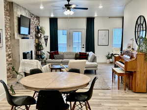 Dining space with light wood-type flooring, a textured ceiling, a fireplace, ceiling fan, and brick wall